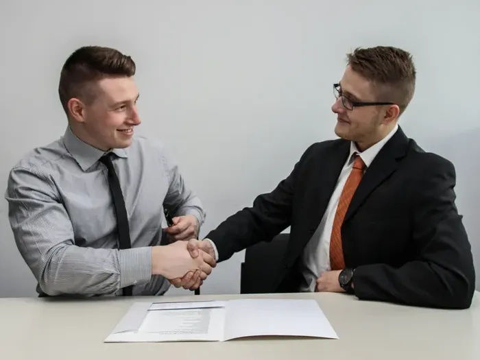 Two professionals shaking hands across a desk after reviewing documents, business agreement in a modern office